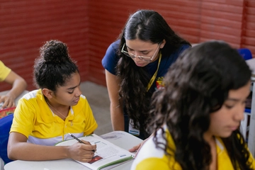 Projeto mantido por doações. Um grupo de meninas com camisas amarelas está sentado à mesa, fazendo a diferença por meio da educação.