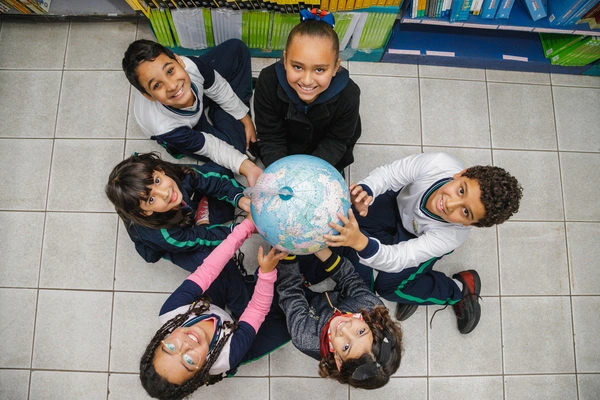 Um grupo de crianças participando da aprendizagem ativa segurando um globo em uma biblioteca.