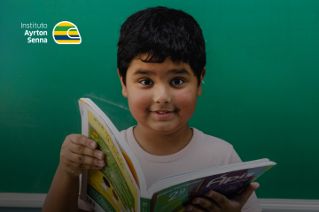 Um menino do Instituto Ayrton Senna segura um livro diante de um fundo verde como parte da campanha de projetos educacionais.