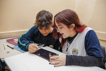 Uma menina e um menino utilizam um tablet para potencializar seu desenvolvimento socioemocional na escola, com foco nas macrocompetências.
