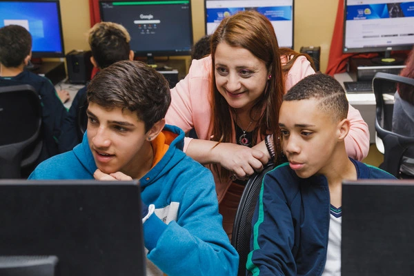 Uma mulher está apoiando um grupo de meninos em um laboratório de informática para desenvolver habilidades de pensamento crítico e aprender sobre notícias falsas.