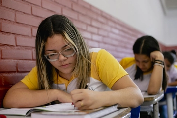 Uma garota de camisa amarela está fazendo um teste em uma sala de aula, demonstrando suas habilidades de pensamento crítico.