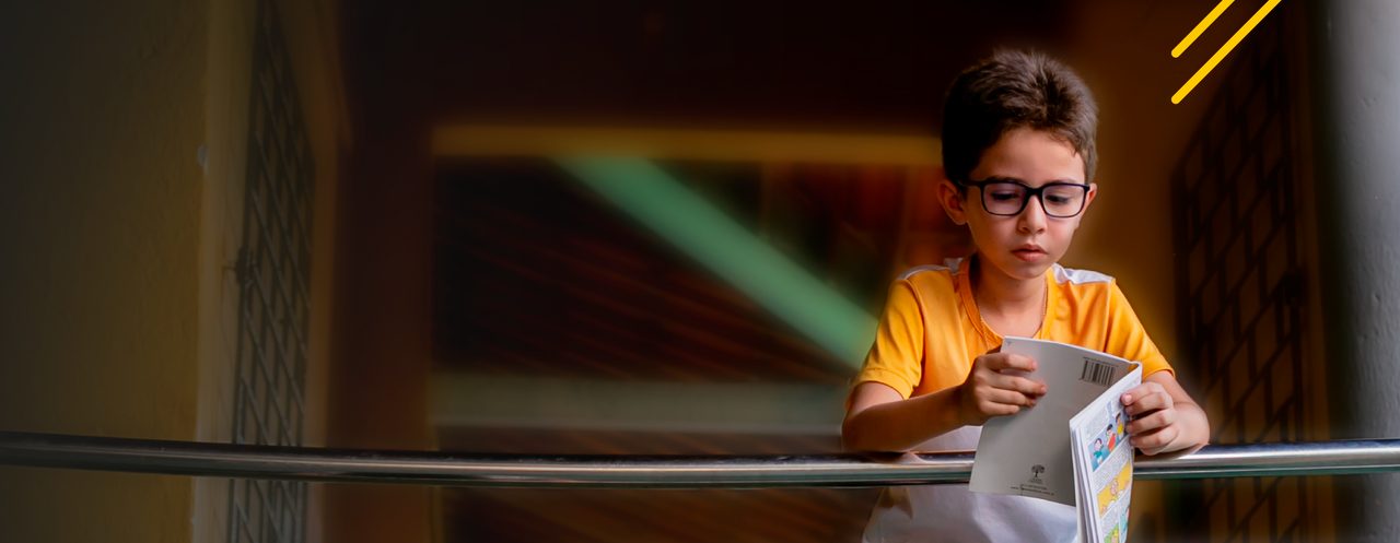 Um menino lendo um livro na grade do Instituto Ayrton Senna.