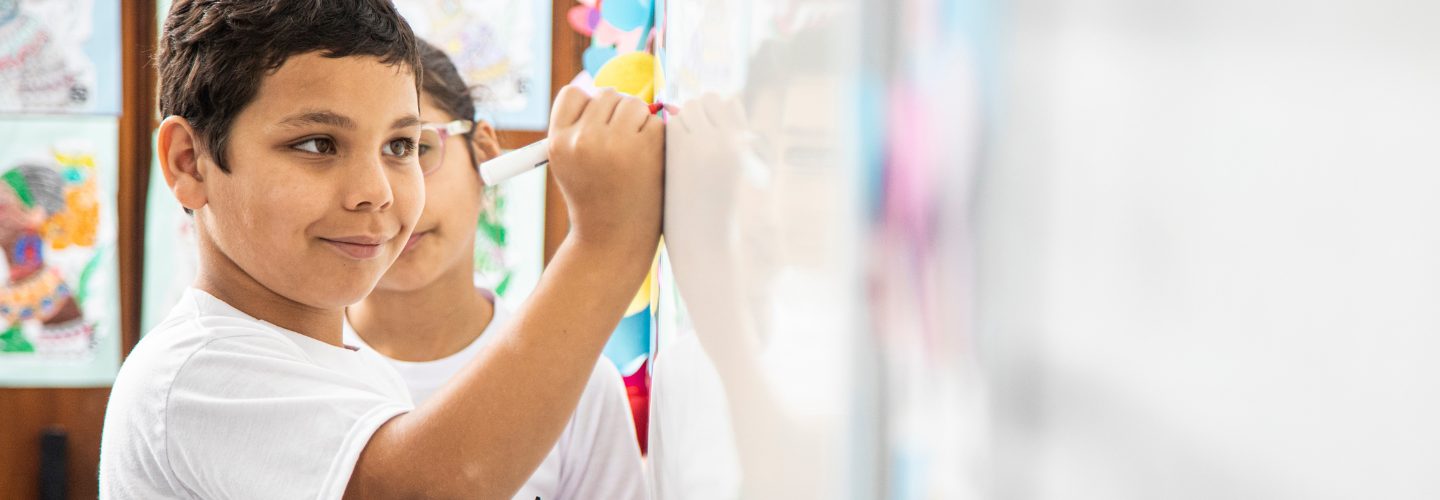 Um menino está desenhando em um quadro branco em uma sala de aula.