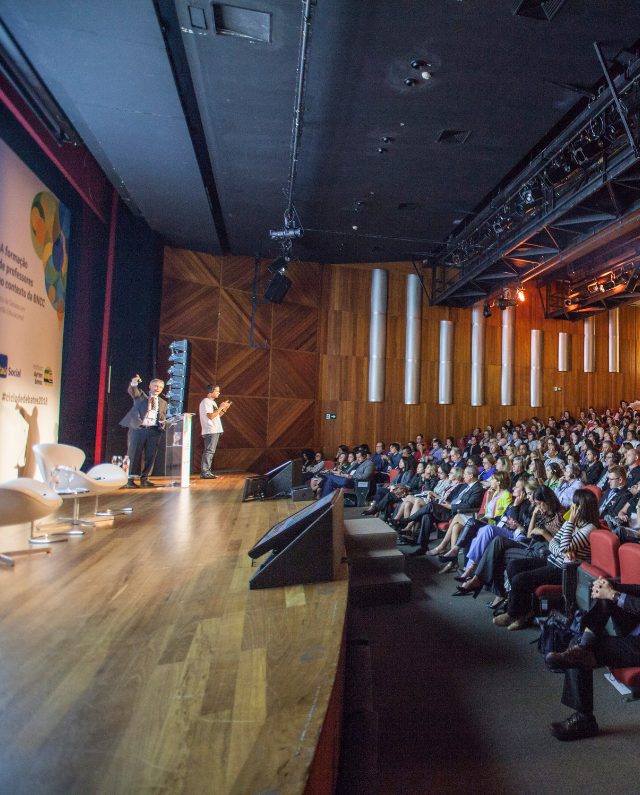 Uma conferência bem concorrida em um auditório moderno com um palestrante apresentando-se no palco para o público.
