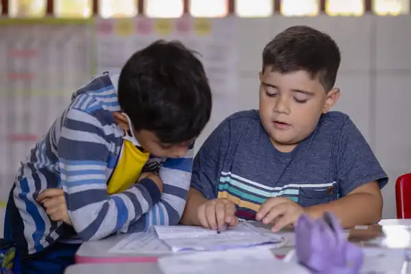 Dois meninos concentrados na elaboração automática do conteúdo de um livro juntos em uma mesa em uma sala de aula.