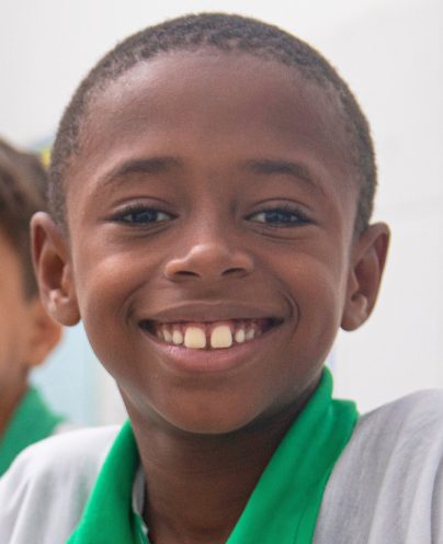 Close de menino sorridente, de cabelo curto, vestindo camisa verde e branca do Cartão Itaú.