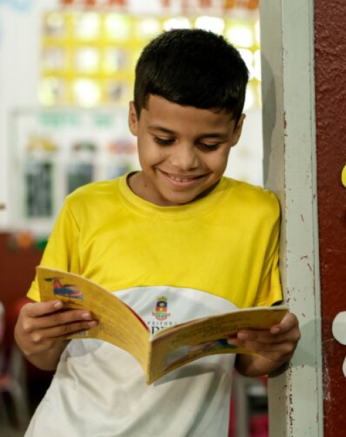 Um jovem de 30 anos com uma camiseta amarela e branca se apoya contra uma parede enquanto lê um livro e sonha no interior.