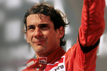 Pessoa com traje de corrida vermelho acenando, olhando para longe, representando o espírito do Instituto Ayrton Senna.