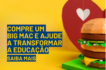 Um modelo de papelão de um sanduíche Big Mac com um coração de papel ao fundo. O texto em português diz: "Compre um Big Mac e ajude a transformar a educação. Saiba mais.