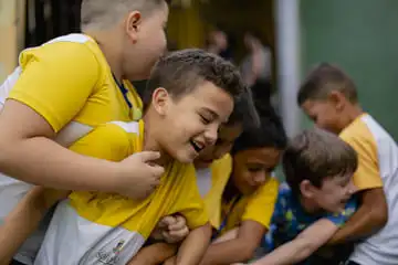 Um grupo de crianças com camisas amarelas e brancas está alegremente reunido, sorrindo e rindo ao ar livre, criando um cenário perfeito para a educação integral.