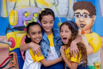 Três crianças sorrindo e se abraçando em uma escola, desenvolvendo suas competências socioemocionais.