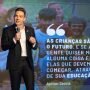 Um homem de terno fala no palco com um microfone no Seminário Alfabetização 360º. Atrás dele, um telão exibe uma frase de Ayrton Senna sobre a educação das crianças e o futuro.