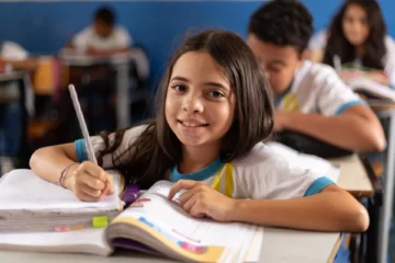 Menina sorridente em sala de aula registrando atividades de aprendizagem, simbolizando como a educação fortalece a sustentabilidade empresarial e impulsiona o ESG.