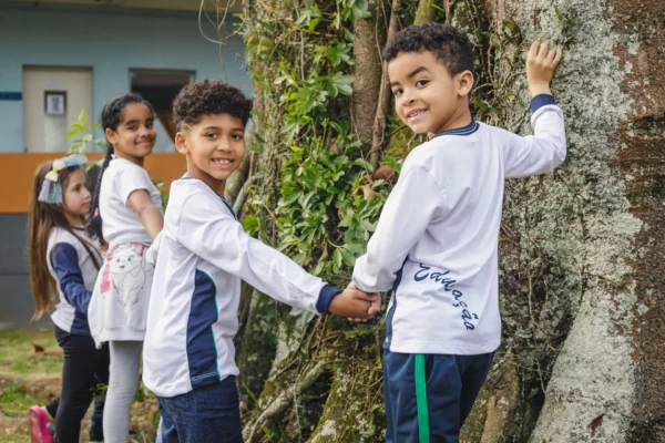 Crianças interagindo com a natureza em atividade escolar, simbolizando como a educação contribui para o desenvolvimento sustentável social e econômico.
