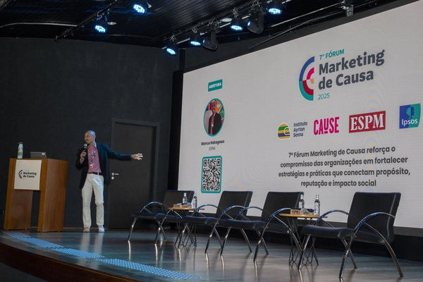 Pessoa no palco apontando para painel escrito 7º Fórum Marketing de Causa