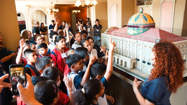 Um grupo de crianças ouve um guia explicando uma grande maquete arquitetônica dentro do Teatro Amazonas.