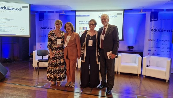Quatro pessoas em pé no palco da EducaWeek 2024, com a identidade visual do Instituto Ayrton Senna visível em faixas e telas de projeção.