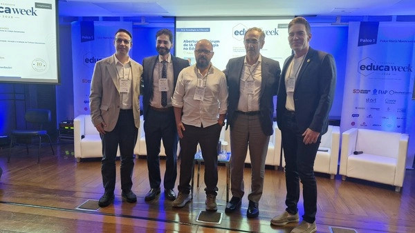 Cinco homens vestidos com trajes profissionais estão alinhados no palco da conferência Educa Week 2026, representando o Instituto Ayrton Senna.