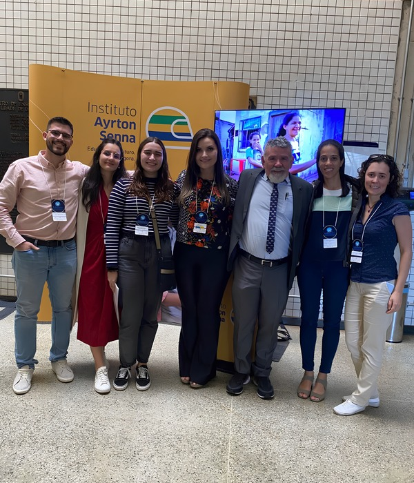 Sete pessoas posam juntas em frente a uma tela digital e a um banner da Cátedra Instituto Ayrton Senna.